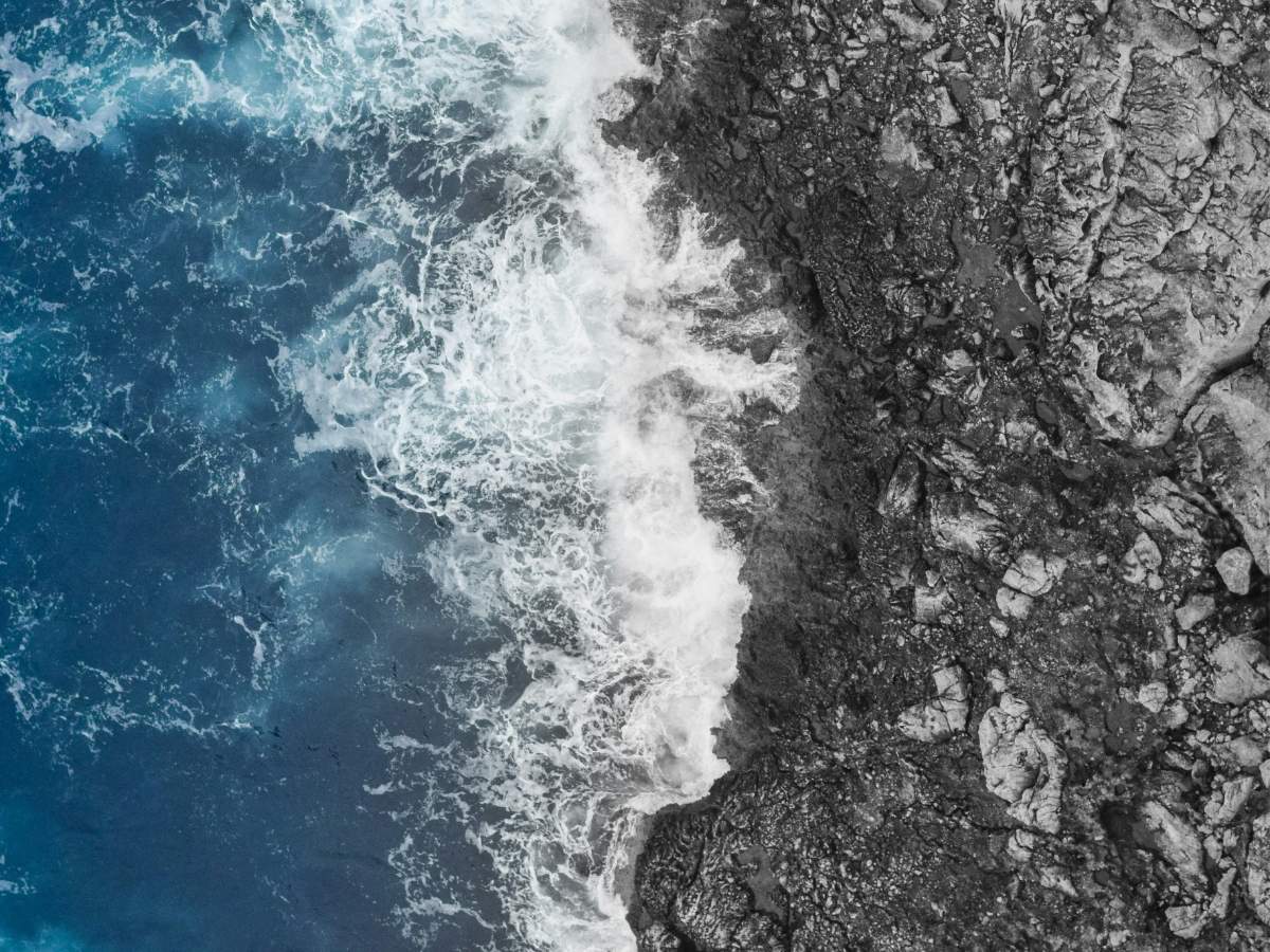Aerial view of ocean waves meeting rocky shore, symbolizing tension and boundaries.